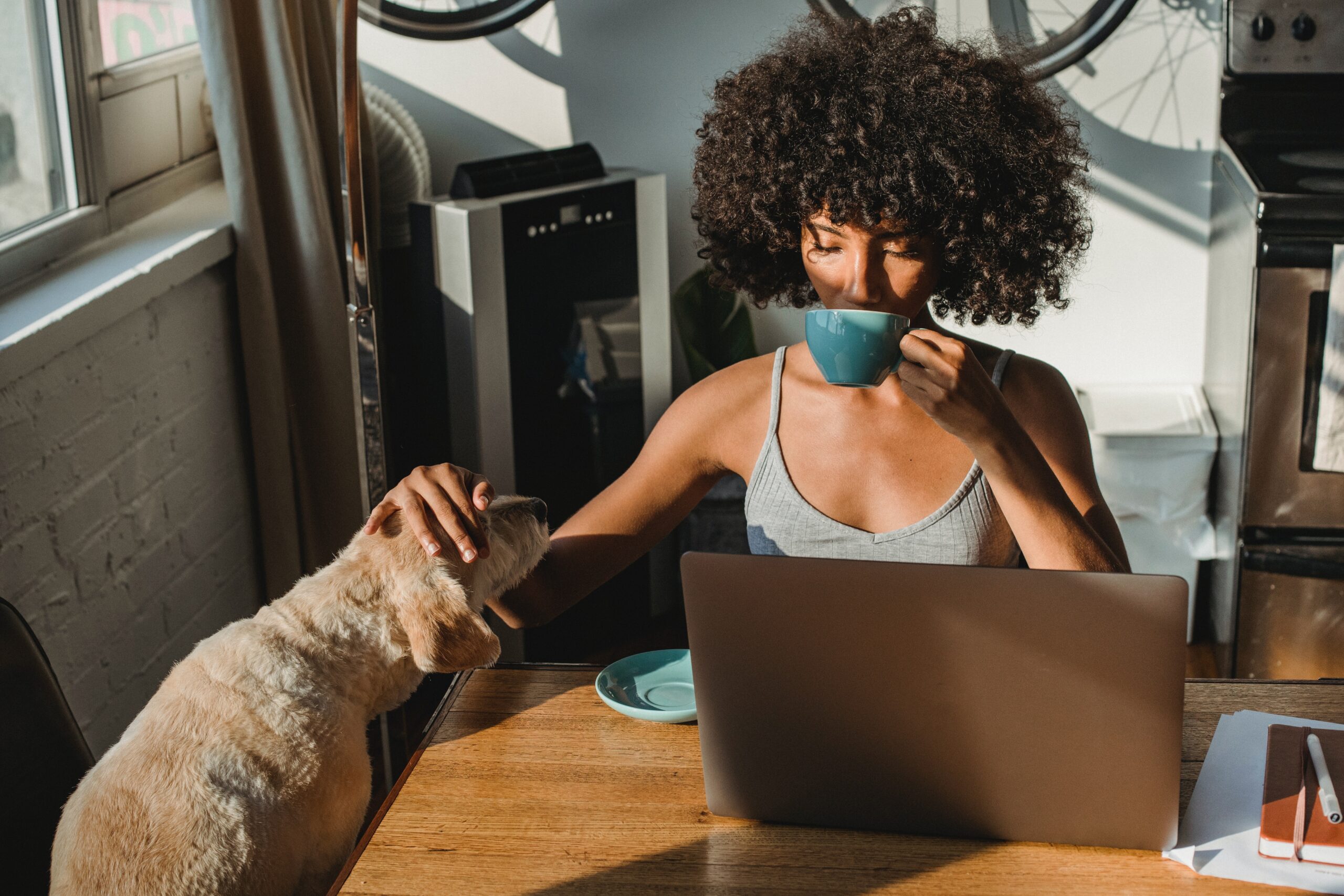 Woman sipping coffee and petting her dog while working from home.